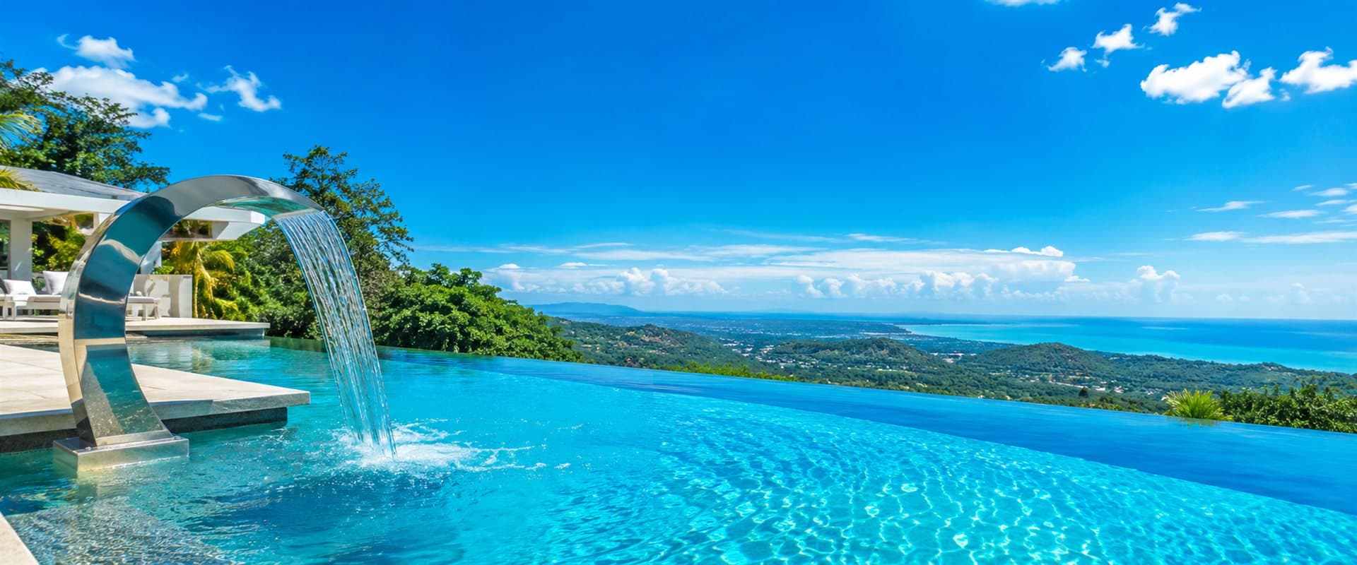 Piscina de borda infinita com cascata de aço inox e vista para o mar em dia ensolarado